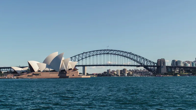 Sydney Opera House and Harbour Bridge across the blue harbour in daylight.